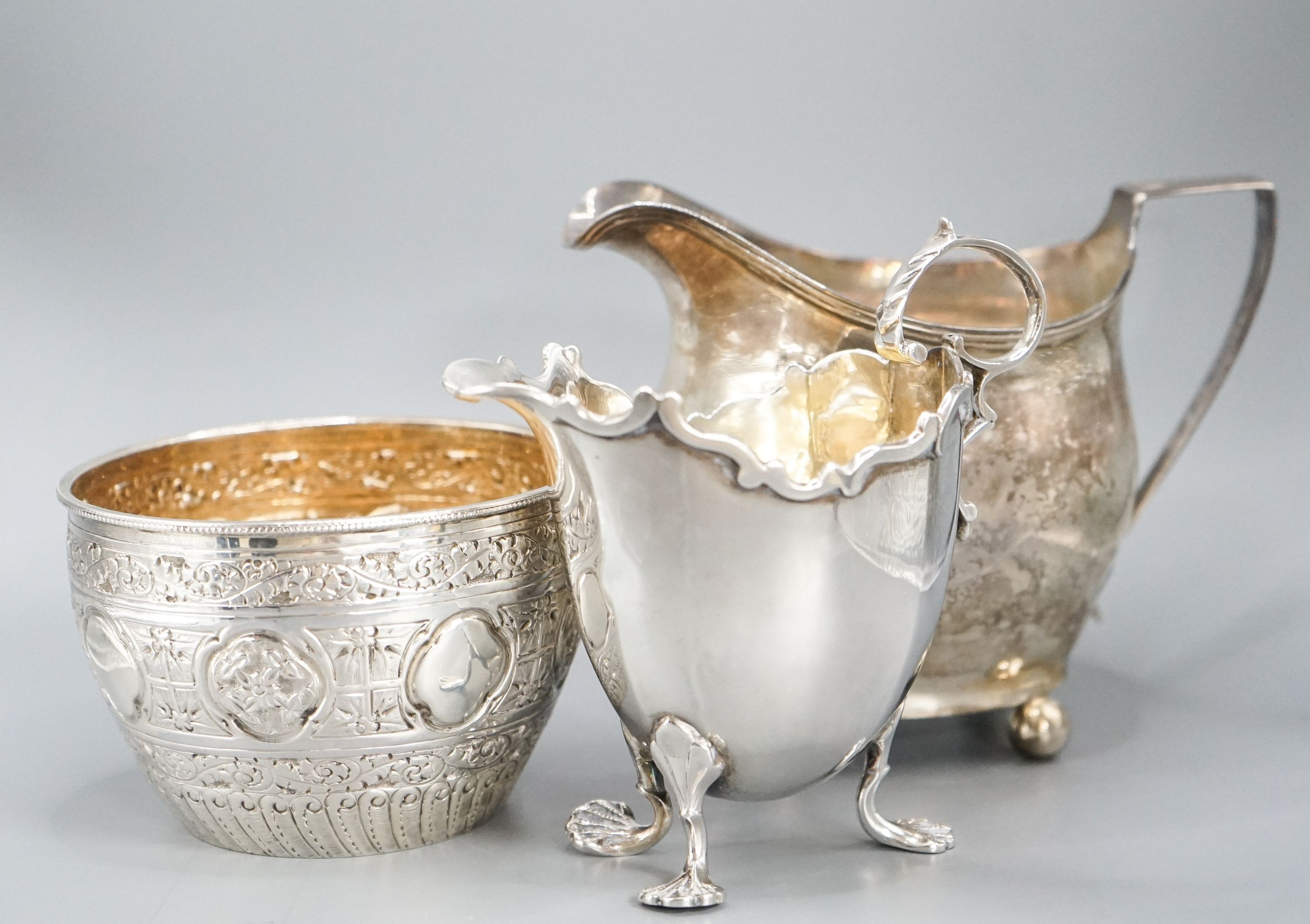 A Victorian repousse silver sugar bowl, a George III silver cream jug and a later silver cream jug